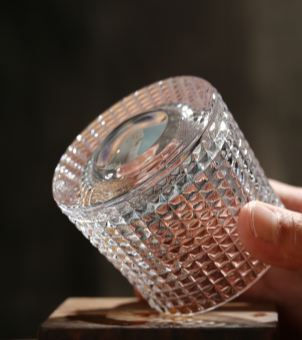 Detailed bottom view of a heavy base whiskey glass held at an angle, showcasing the thick spherical glass bottom, tapered cone shape, and diamond cut waffle pattern for commercial barware supply.