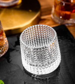 High-angle shot of an empty clear textured drinkware tumbler showcasing excellent clarity and a hobnail waffle pattern, placed on a dark slate tray for commercial barware hospitality sourcing.