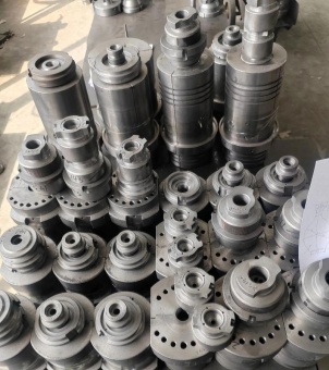 The factory workshop is filled with a dense and orderly array of various industrial metal molds. These steel molds are cylindrical or multi-tiered stepped structures, with machined textures, grooves, and positioning holes on their surfaces. A corner of a white sheet of paper with design drawings is visible on the right side. The entire scene showcases the production preparation process for glassware or molding industries.
