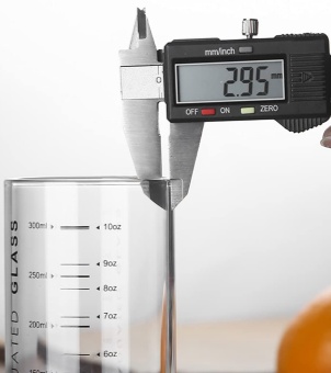 The image shows the thickness of a glass being measured using vernier calipers. The glass has a capacity label, and the image illustrates the calibration of the accuracy of the glass measuring tool.
