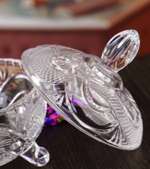 A close-up of the lid of the crystal glass candy jar shows the olive-shaped three-dimensional handle and the delicate embossed edge.