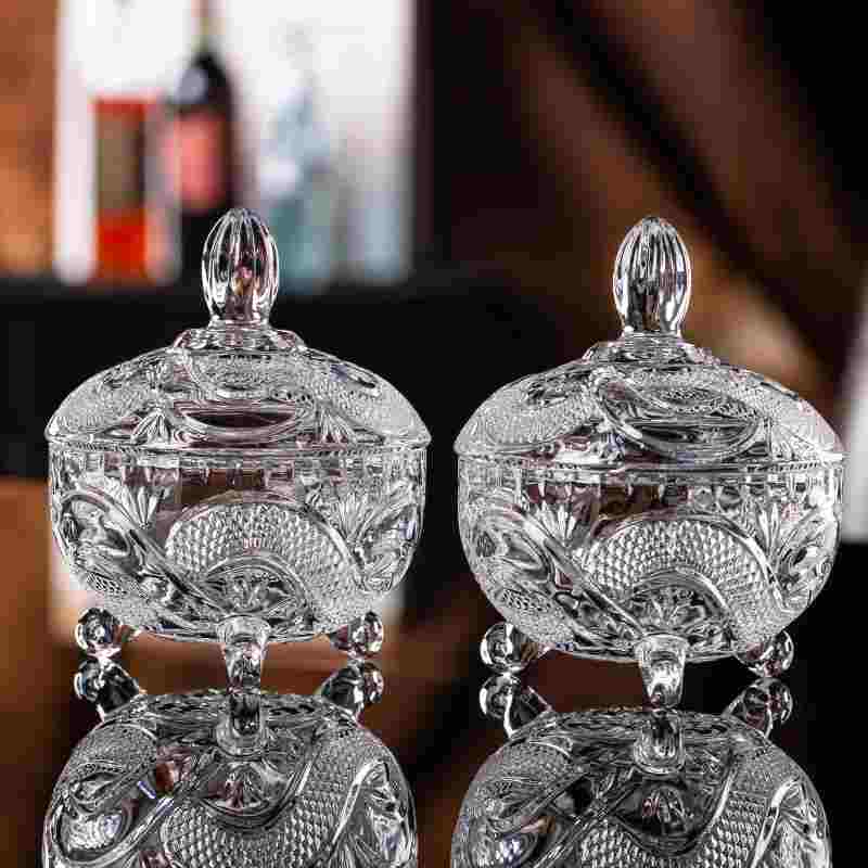 Two vintage-style three-legged crystal glass candy jars are placed symmetrically on a black high-gloss tabletop.