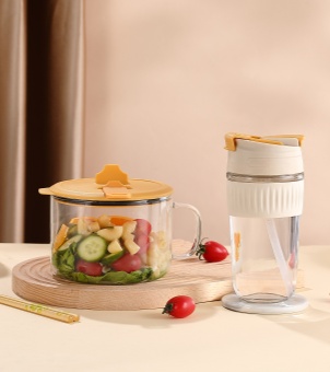 A Xinghuo Glass transparent salad bowl and a portable water bottle with a silicone sleeve are placed on a wooden countertop.