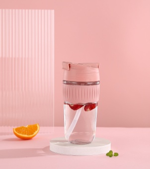 The Xinghuo Glass travel mug, displayed against a pink background, features a textured silicone sleeve designed to prevent burns