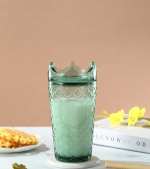 A dark green crown-capped Xinghuo Glass sits quietly on the table, containing a light green beverage, against a backdrop of yellow flowers.