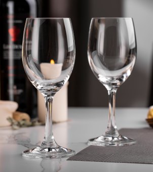 Two Xinghuo Glass 100% lead-free, high-transparency crystal wine glasses stand on the dining table, sparkling clear and reflecting light beautifully.