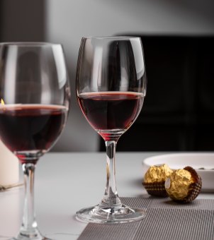 Two Xinghuo Glass crystal goblets filled with red wine stand side by side on the dining table, showcasing their elegant and durable appearance.
