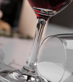 A close-up of the Xinghuo Glass shows its seamless, stretched stem and thickened, sturdy base, with another wine glass placed horizontally beside it.