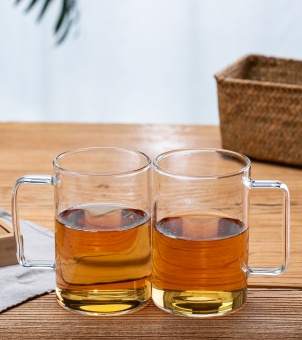 Two Xinghuo Glass heat-resistant borosilicate glass mugs filled with hot tea are placed stably on the wooden table.