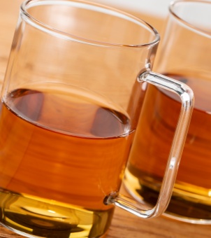 A close-up view of the square heat-insulated handle of the Xinghuo Glass transparent mug, filled with golden-yellow tea.