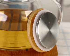 Close-up image of the bamboo lid and stainless steel inner core of a heat-resistant glass teapot.