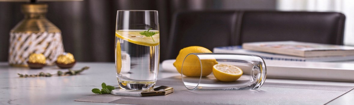 xinghuo-260ml-crystal-highball-lemon-mint-scene Tall clear crystal highball glass with lemon and mint on a marble tabletop, a second empty glass lying beside it